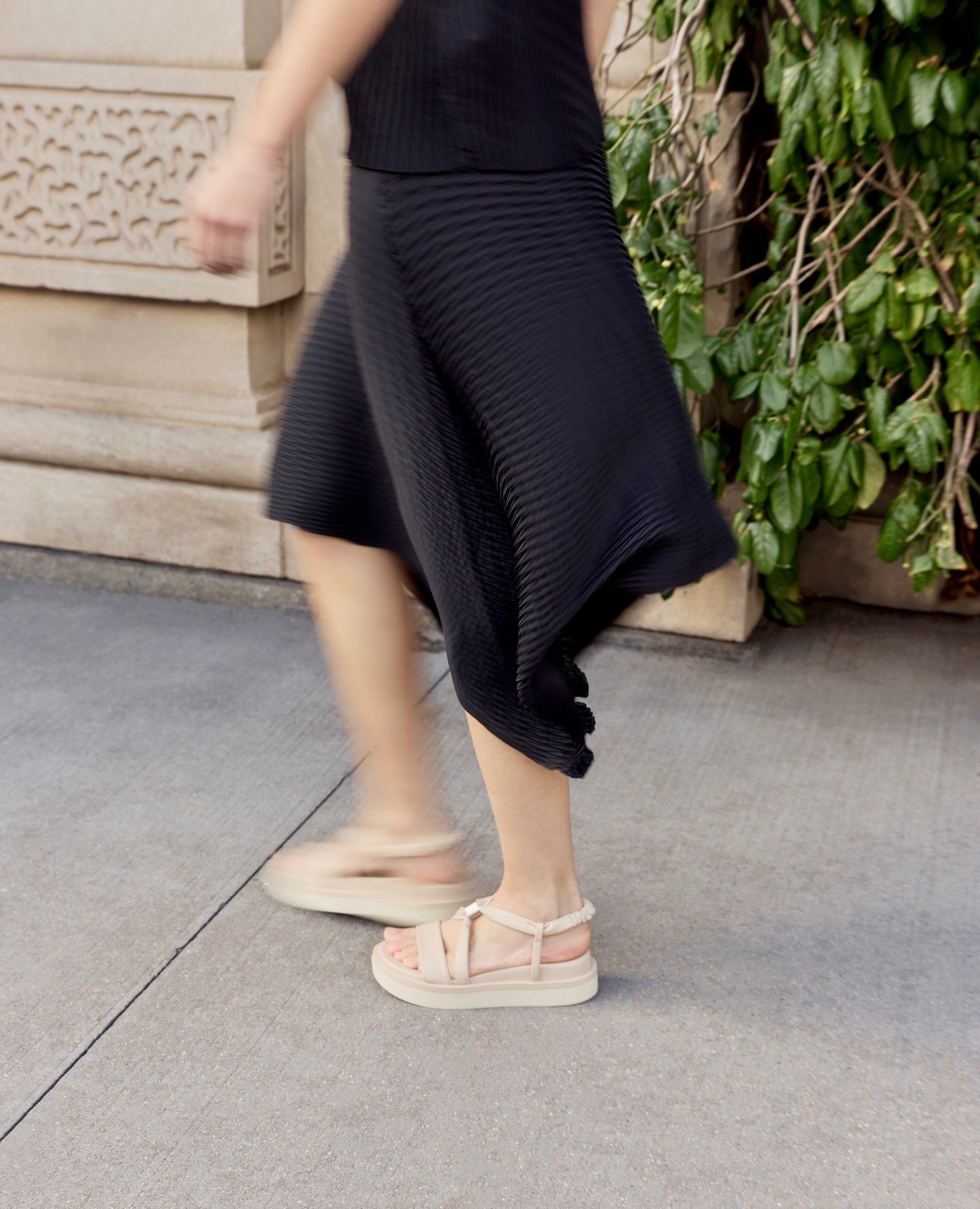 A woman walks down a New York City wearing black skirt and the best selling Coclico Orlando footbed platform sandals in a warm pale grey. The shoes are for a 10,000 step day.
