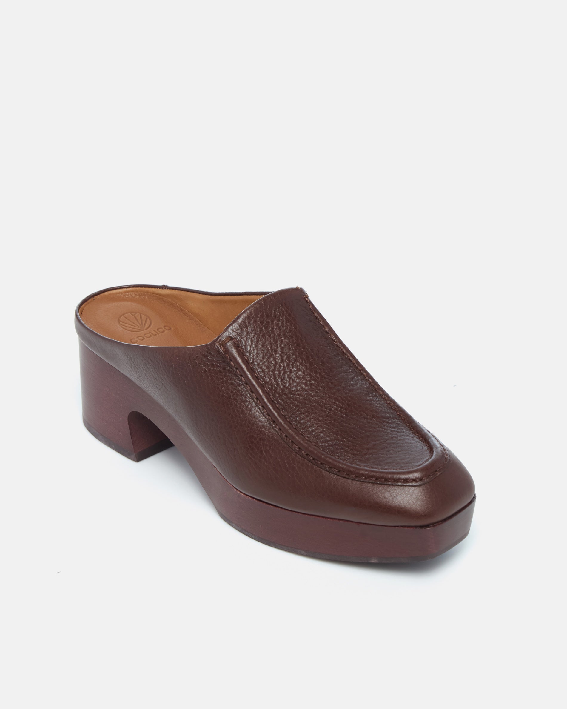 Coclico Qadira Clog in Castagno leather, angled view of a closed toe clog mule on a mahogany platform