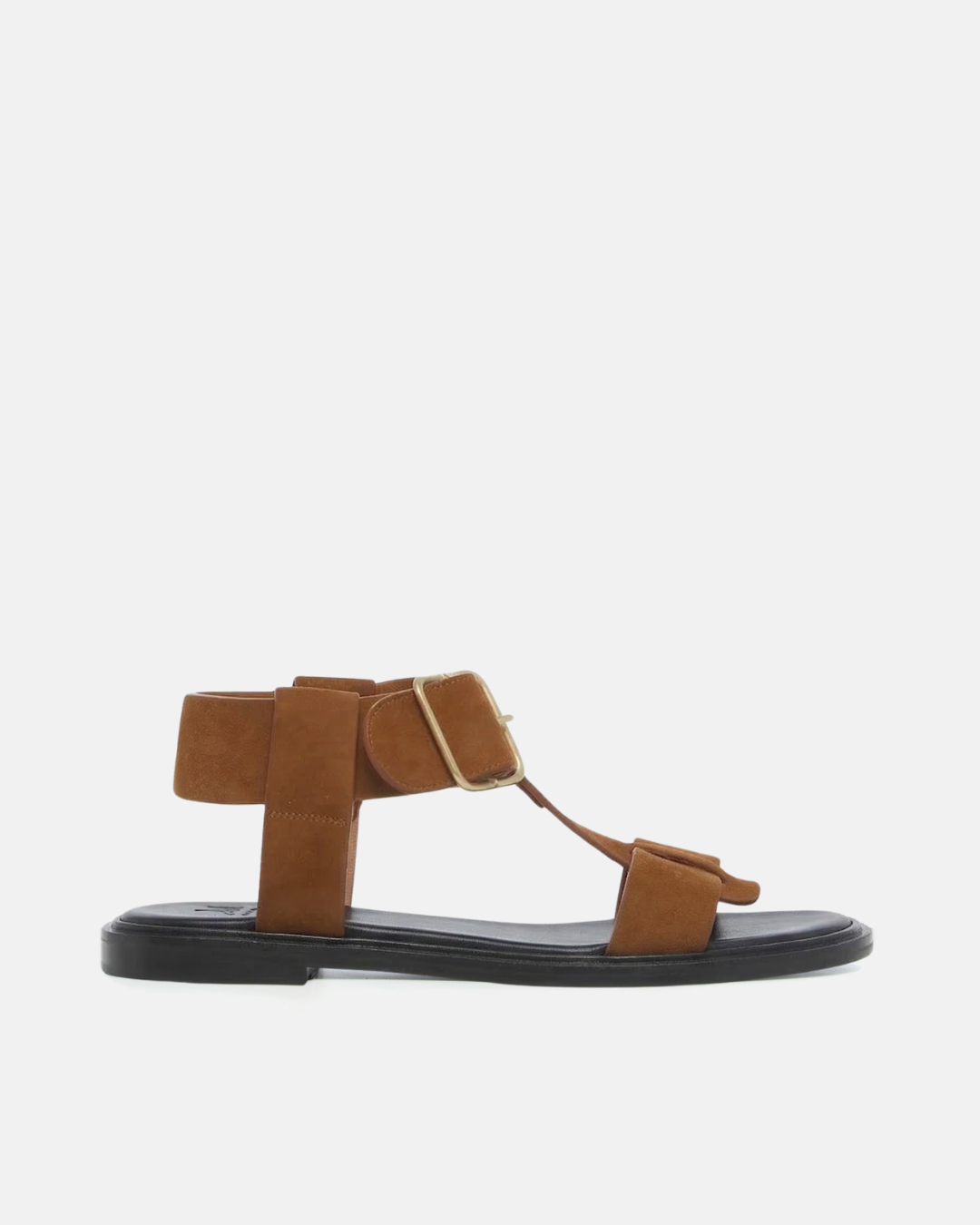 Side view of a brown suede T-strap sandal with wide straps, oversized buckle, cushioned leather footbed, and substantial sole