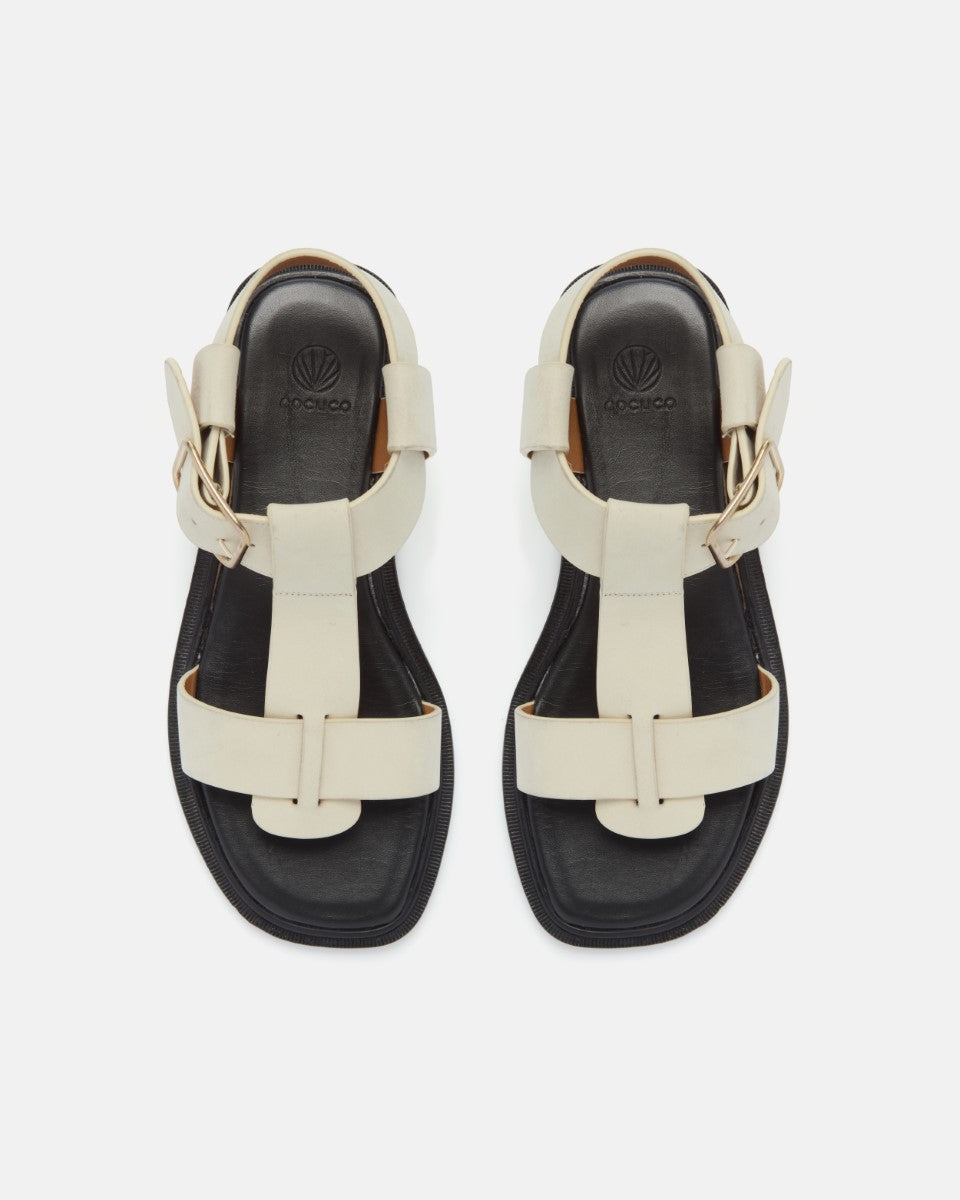Top view of white nubuck leather T-strap sandals with wide straps, oversized buckle, cushioned leather footbed, and substantial sole on a white background.