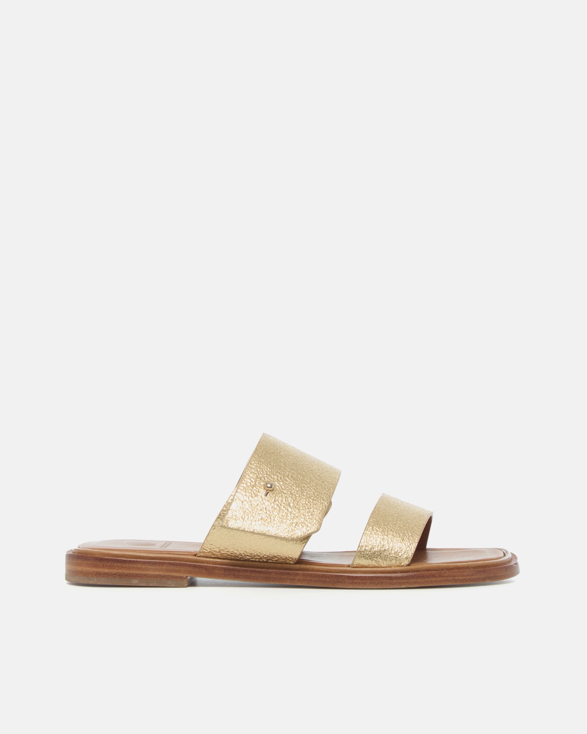 Side view of a gold metallic leather slide sandal with two wide straps, a subtle metal peg detail, cushioned leather footbed, and flat leather sole