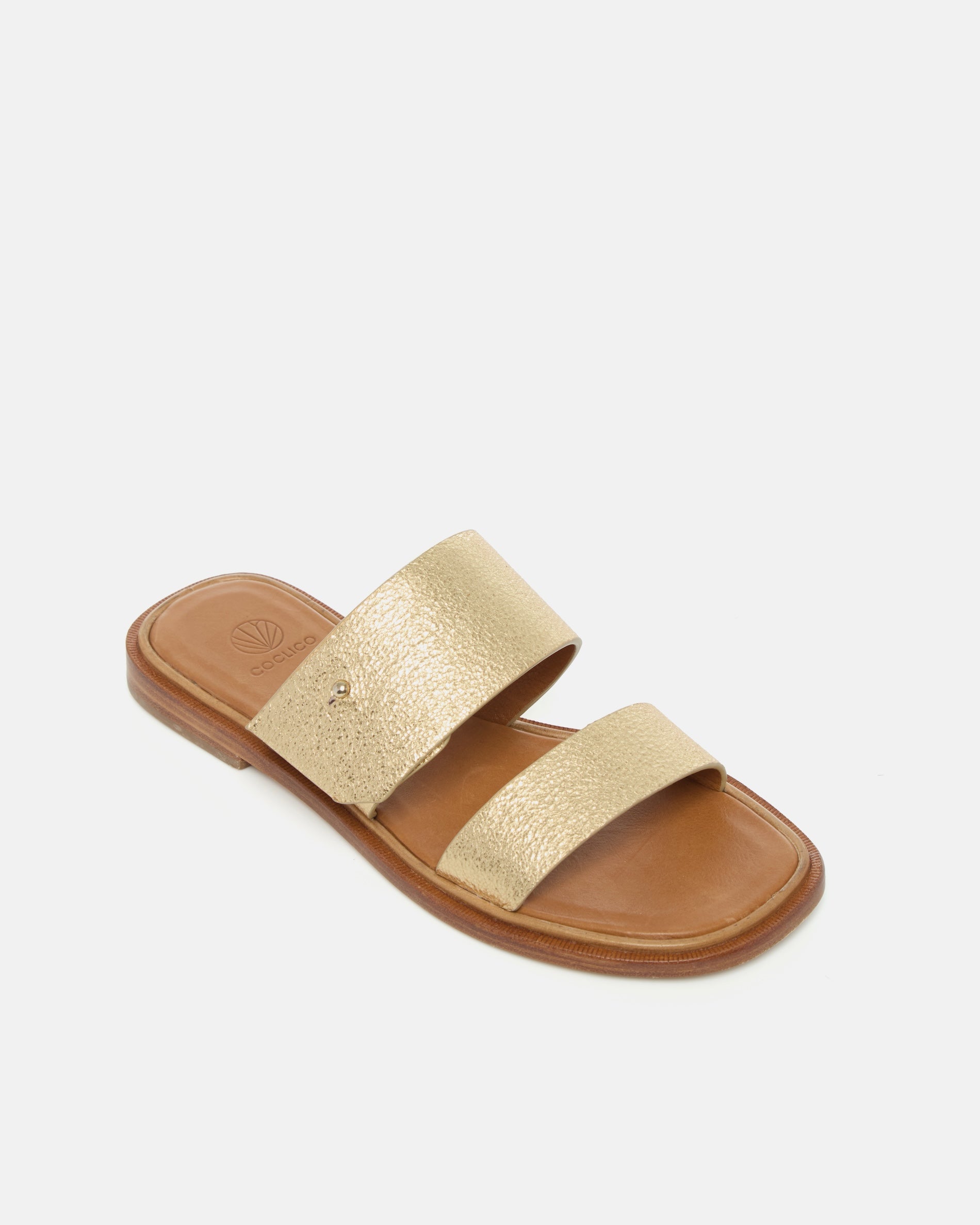 Angled view of a gold metallic leather slide sandal with two wide straps, a subtle metal peg detail, cushioned leather footbed, and flat leather sole