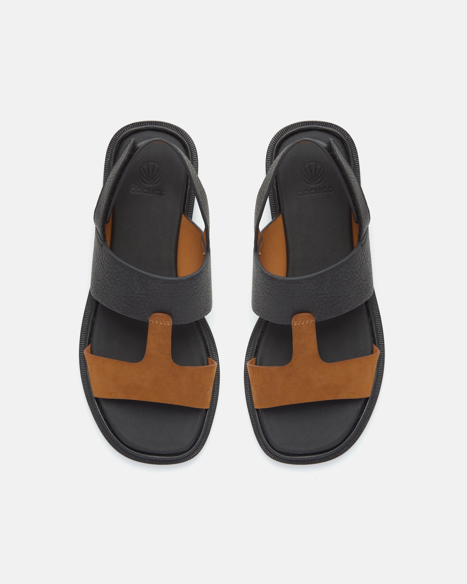 Top view of a two-tone leather slide sandal with wide black and brown straps, slim slingback strap, cushioned leather footbed, and flat sole.