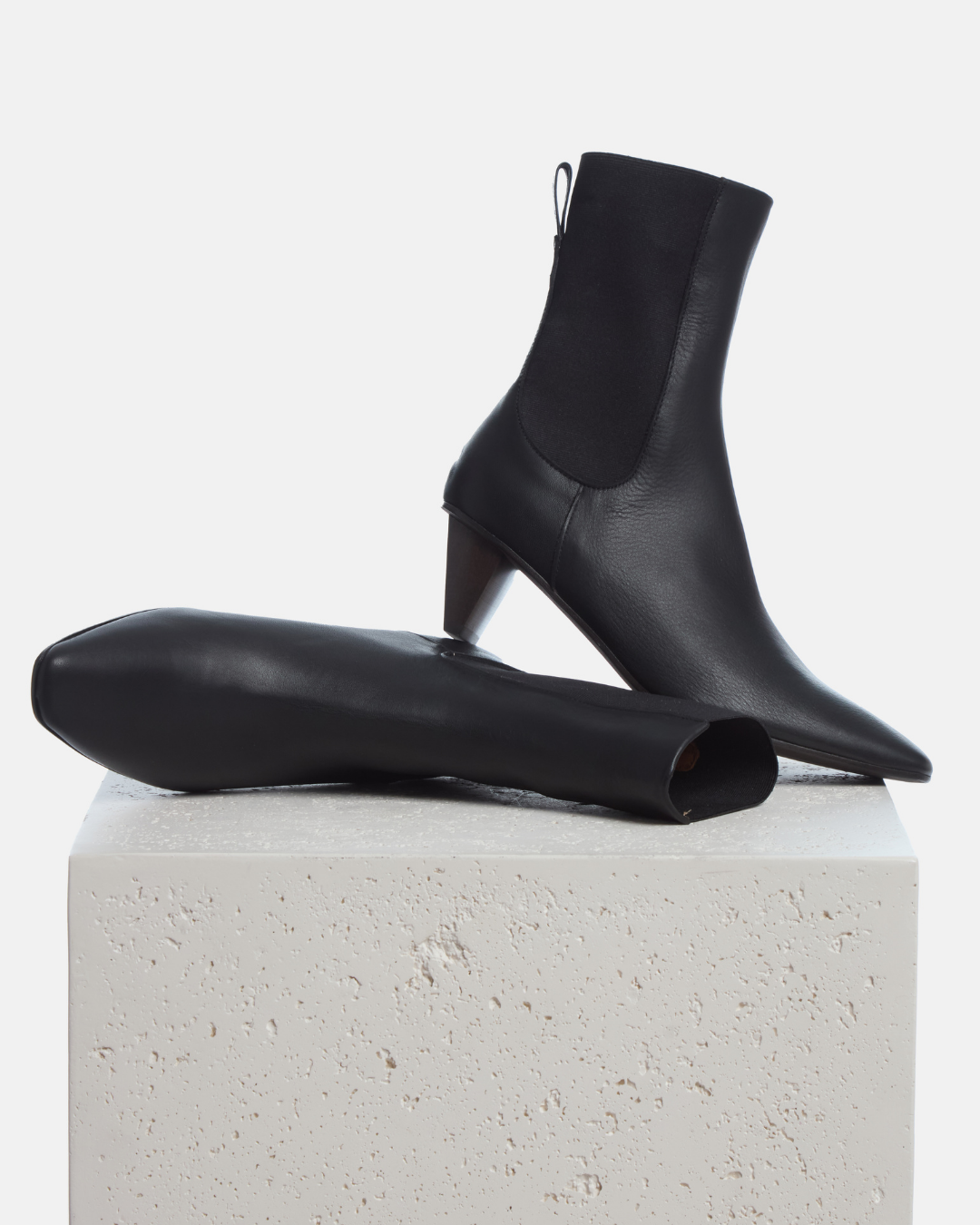 Coclico Suttner Boot in black leather, pointed toe Chelsea boots with cone heels styled on a stone plinth