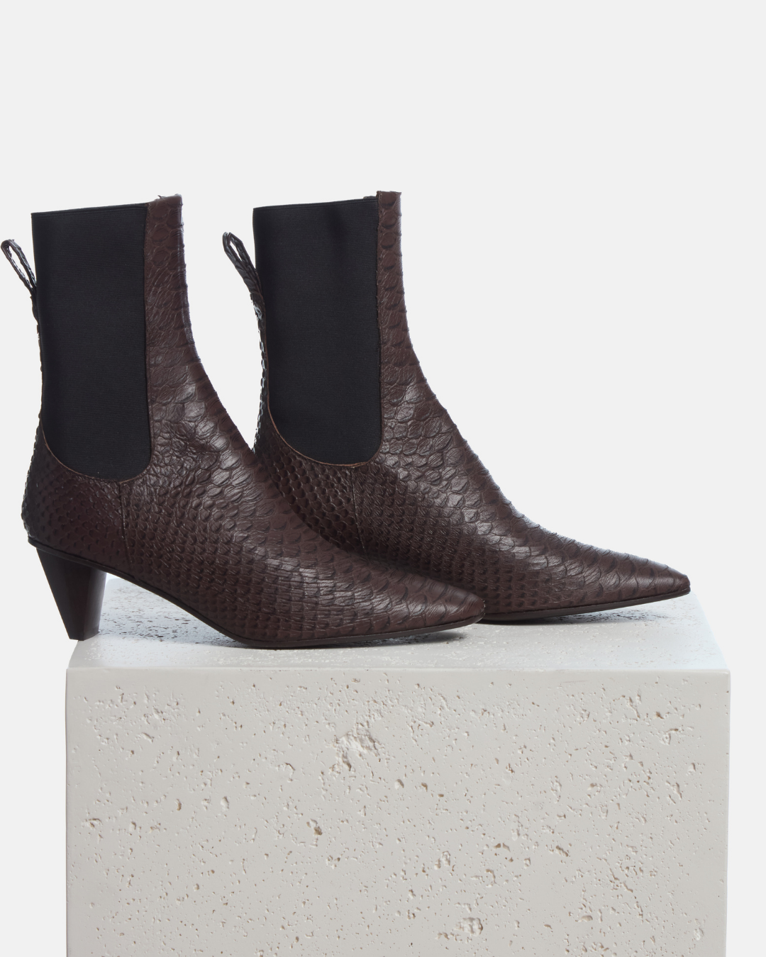 Coclico Suttner Boot in espresso snake embossed leather, pointed toe Chelsea boots with cone heels styled on a stone plinth