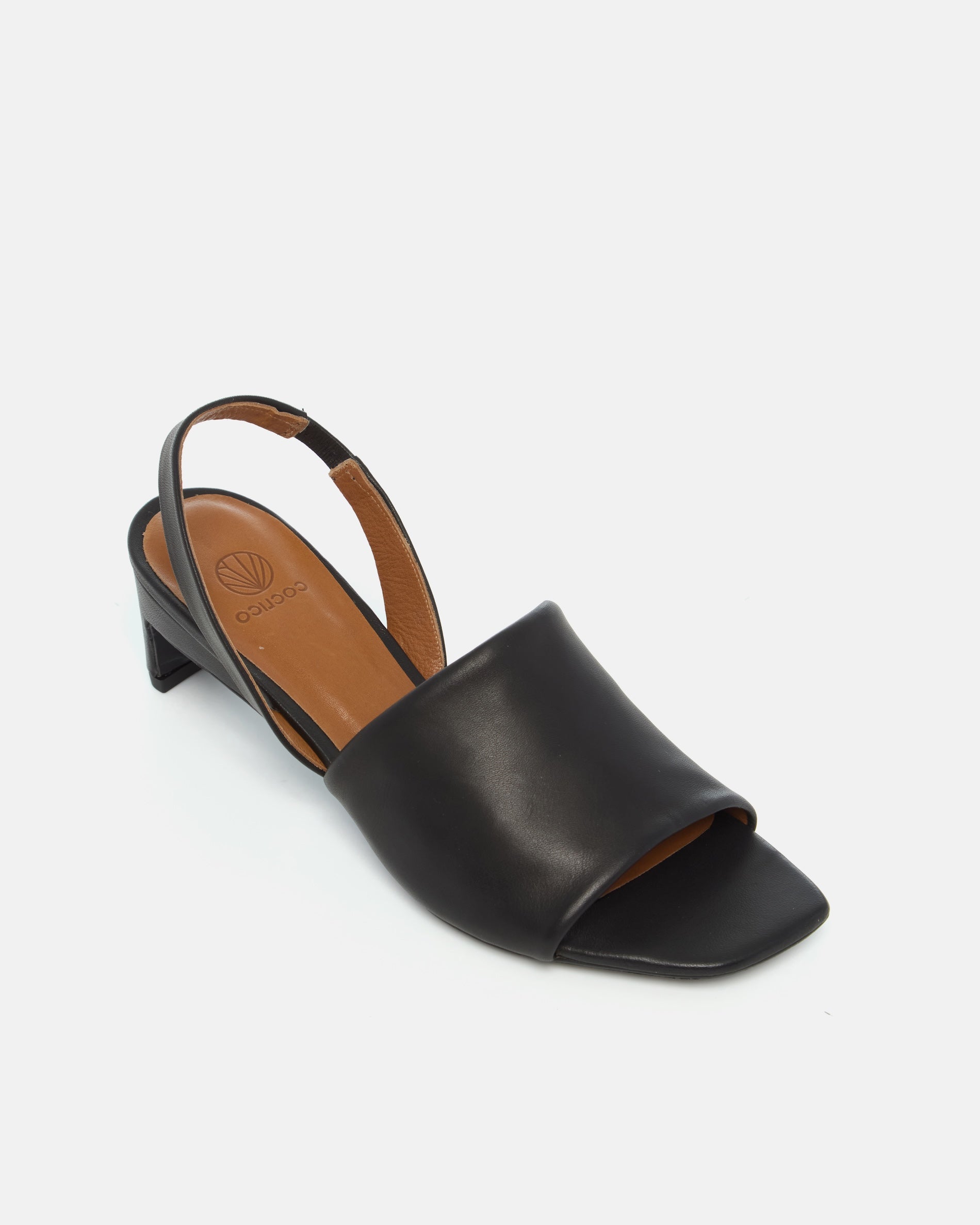 Angled view of a black leather mid-heel sandal with a wide band, delicate slingback, squared toe, and sculptural block heel