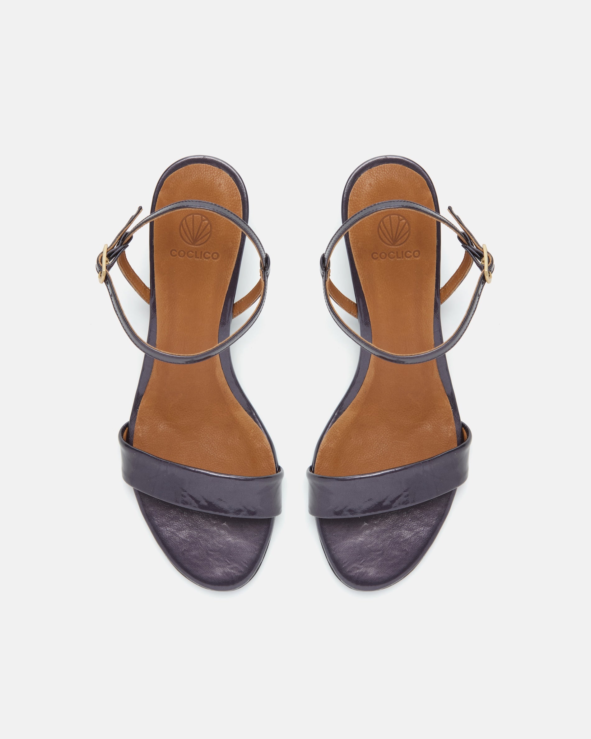 Top view of a black pearl patent leather sandal with a slim strap, ankle buckle, and sculptural wooden demi-wedge