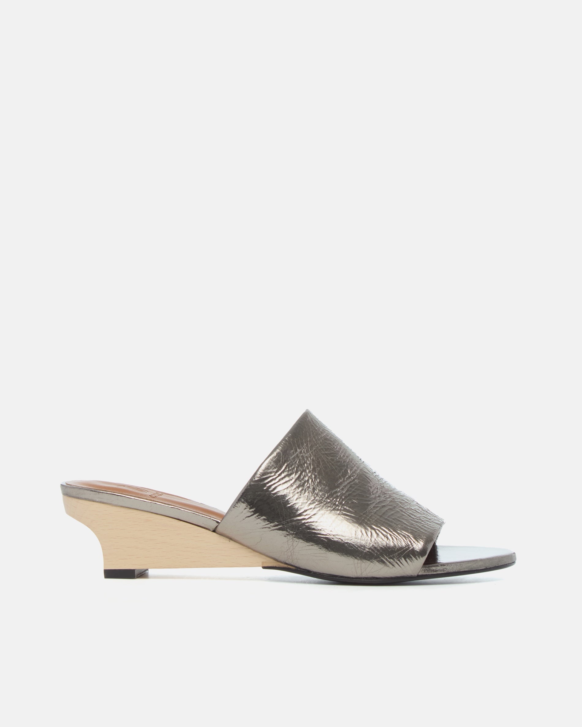 Side view of a pewter metallic slide sandal with a wide crinkled leather band and sculptural wooden demi-wedge
