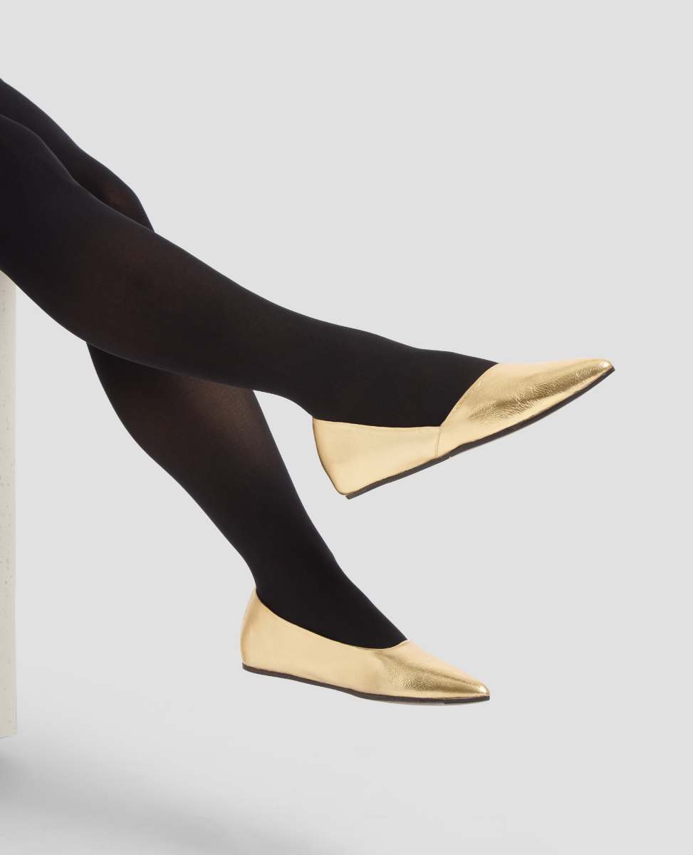 Gold flats worn with black tights on a light gray background