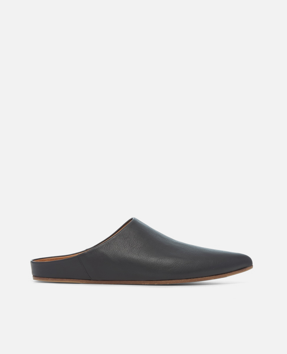 Side view of a black pointed-toe leather mule with a slight built-in wedge and clean minimalist silhouette on a white background