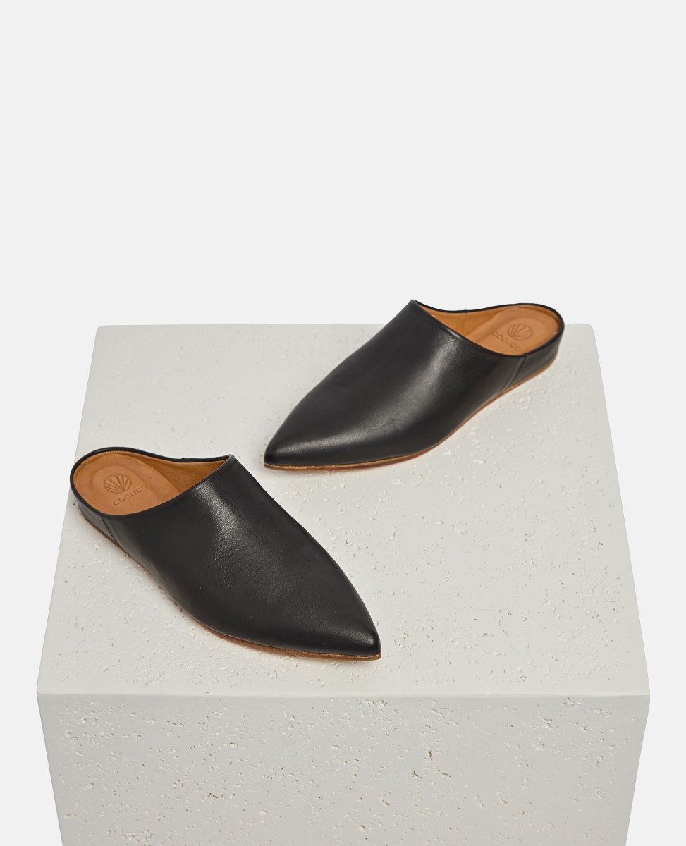 Pair of black leather slippers on a white cube