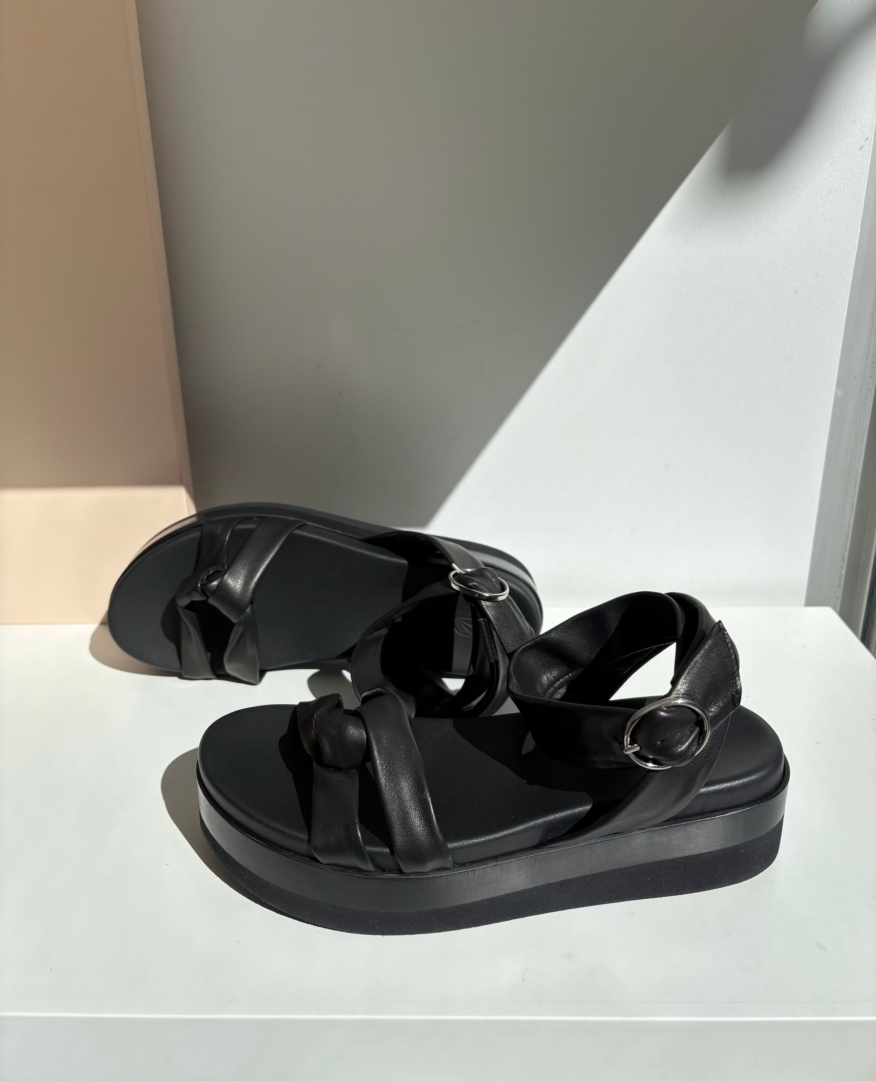 Black sandals with thick, cushioned soles, featuring wide straps and silver buckle accents, crafted from smooth leather with a matte finish.