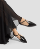 Black pointed-toe flats worn with a long black skirt on a light gray background 5