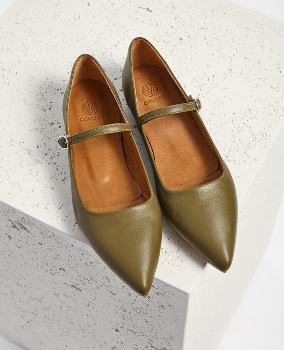 Olive green leather Mary Jane flats with pointed toes, a slim adjustable strap with a silver buckle, and a smooth, polished finish.