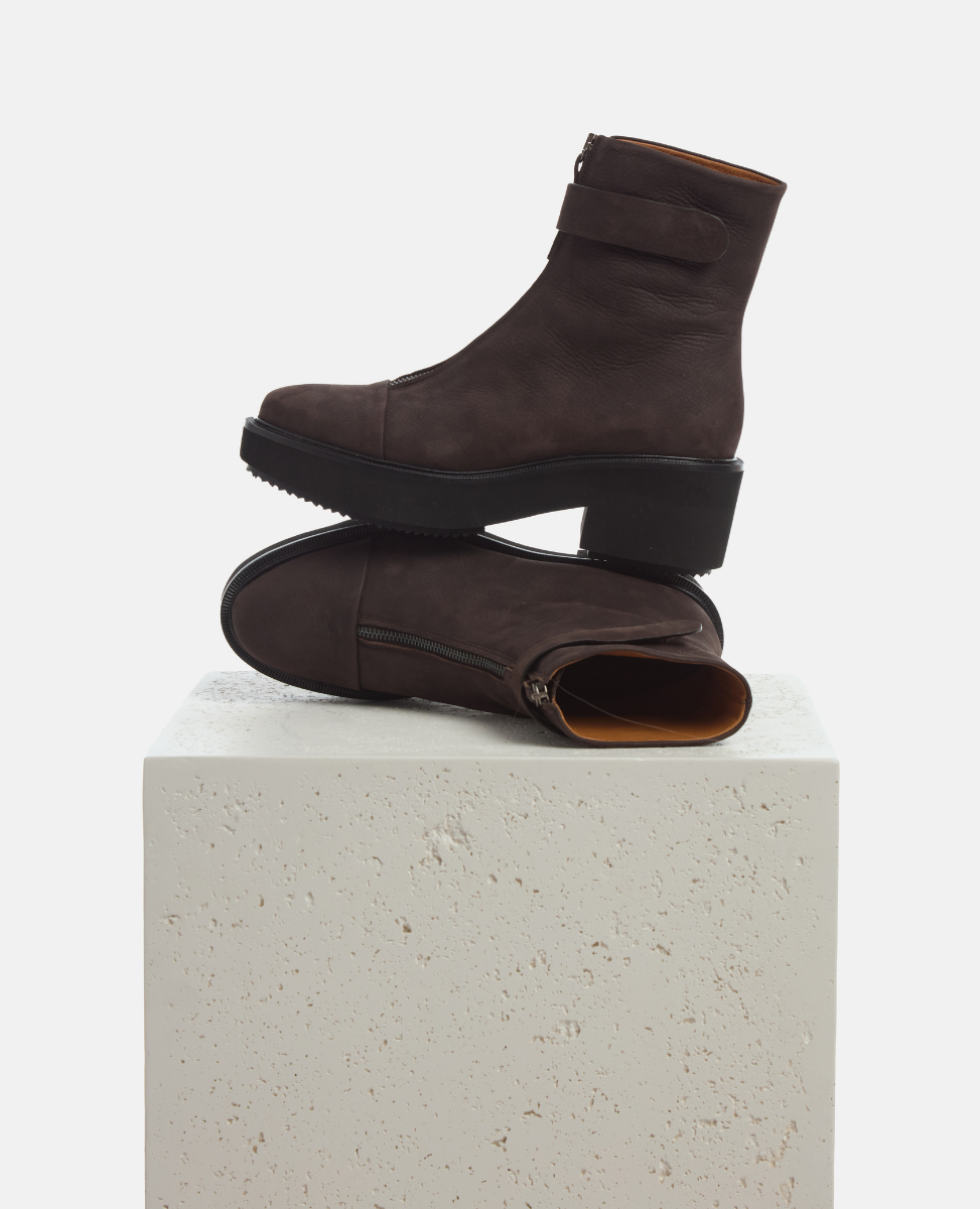 Pair of brown boots stacked on a white pedestal with a light gray background