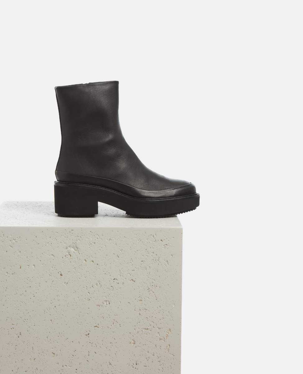 Black ankle boot on a light gray pedestal against a white background