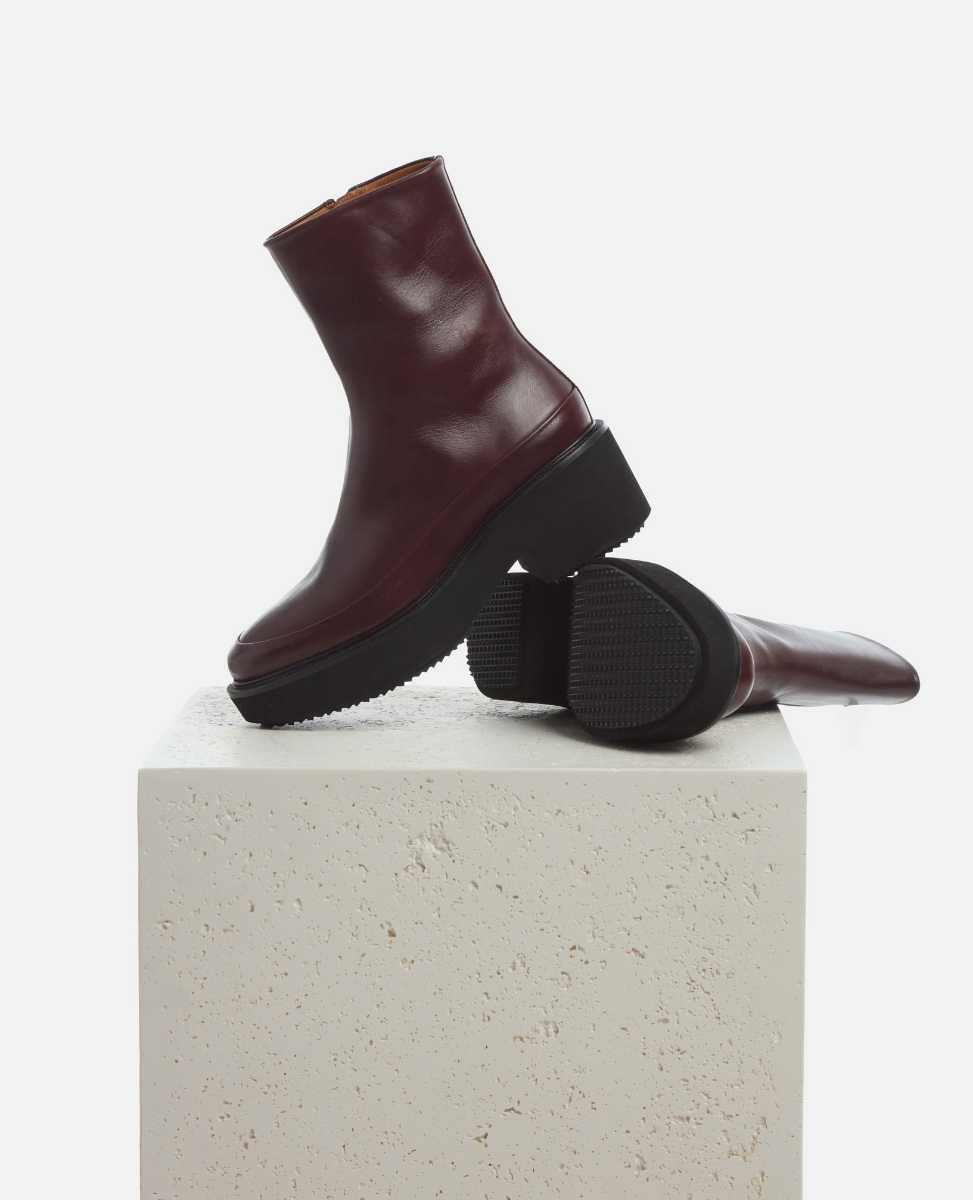 Pair of maroon boots on a light gray pedestal against a white background