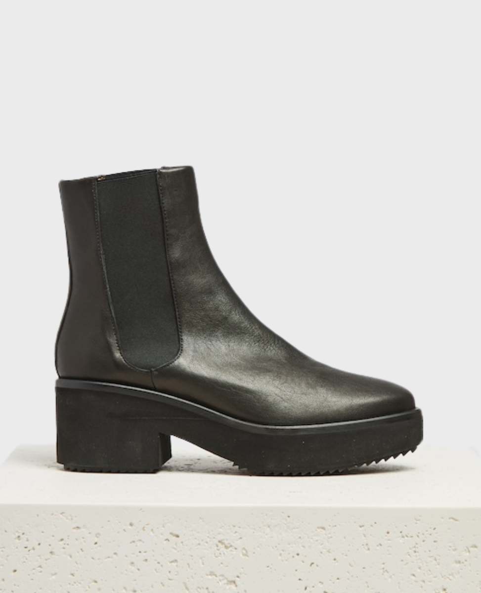 A sleek, black leather chelsea boot with a chunky heel, elastic side panels, and a smooth, polished finish, featuring a slightly rounded toe and a textured rubber sole.