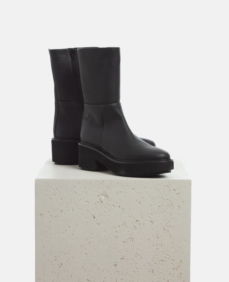 Black boots on a light gray pedestal against a white background