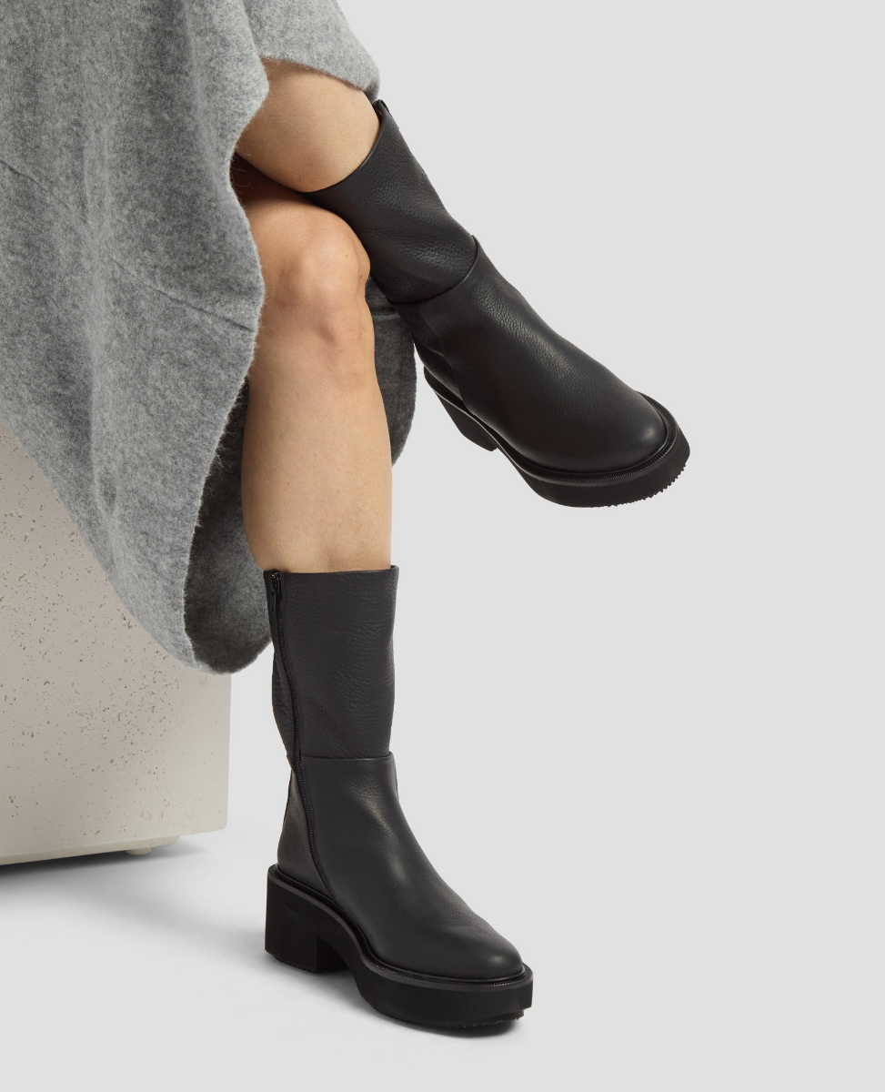 Person wearing black knee-high boots on a light gray background