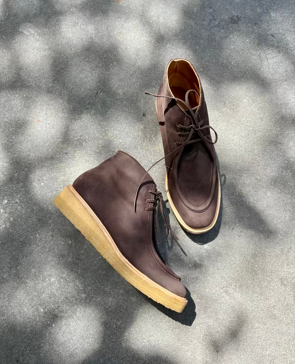 Pair of brown leather chukka boots with crepe soles on a textured gray surface