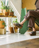 Woman sitting and wearing the Moska Wedge in Deep Sea leather a Huarache inspired cork wedge with a woven leather band across foot, slingback strap. 5