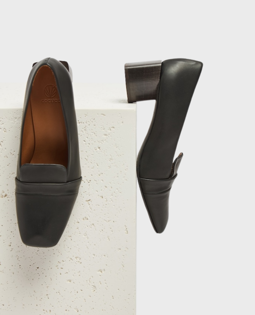 A pair of black leather loafers with a square toe, block heel, and a smooth, polished finish, featuring a subtle logo embossed on the insole.