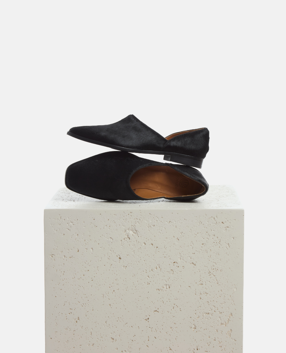 Black flat shoes on a light gray pedestal against a white background