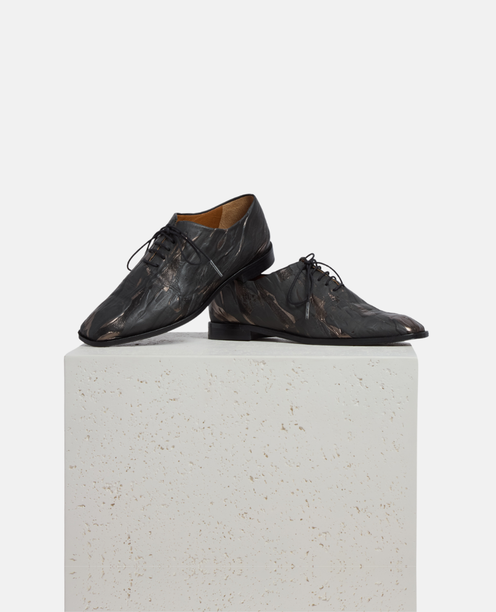 Pair of black leather shoes on a white pedestal with a white background