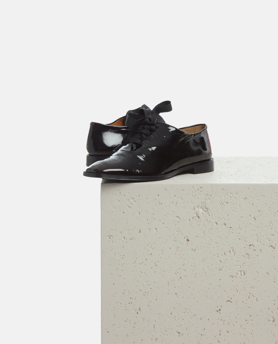 Black patent leather shoes on a light gray surface with a white background