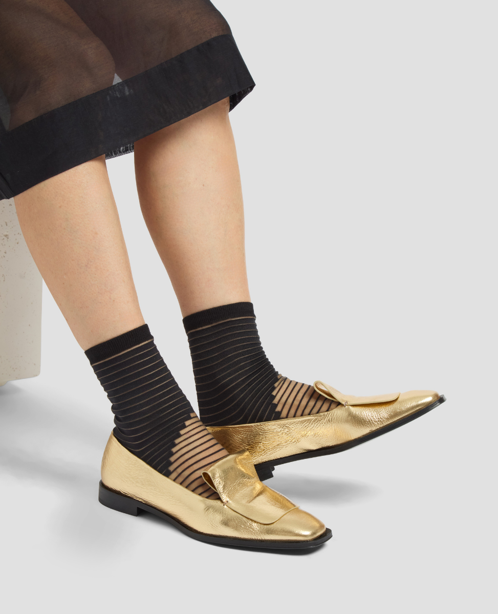 Gold loafers worn with black socks on a neutral background