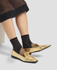 Gold loafers worn with black socks on a neutral background 6