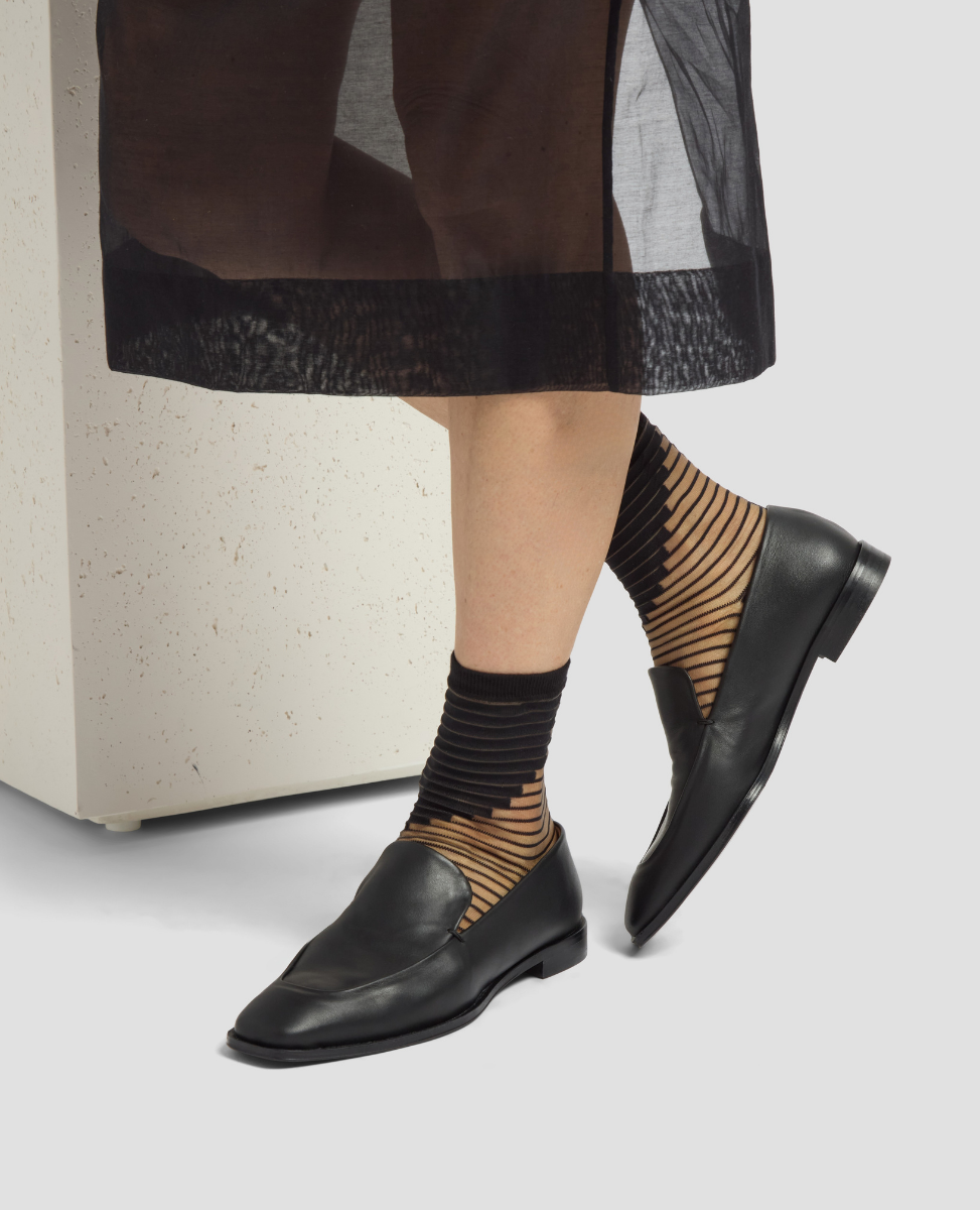 Person wearing black loafers and striped socks on a neutral background