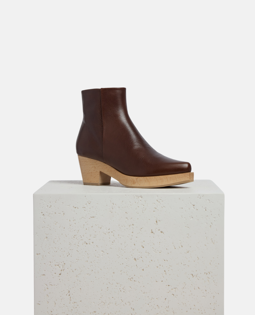 Brown leather ankle boot on a white pedestal with a white background