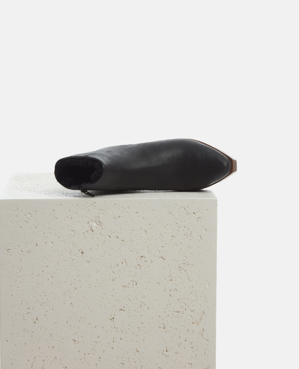Black leather ankle boot on a light gray surface with a white background
