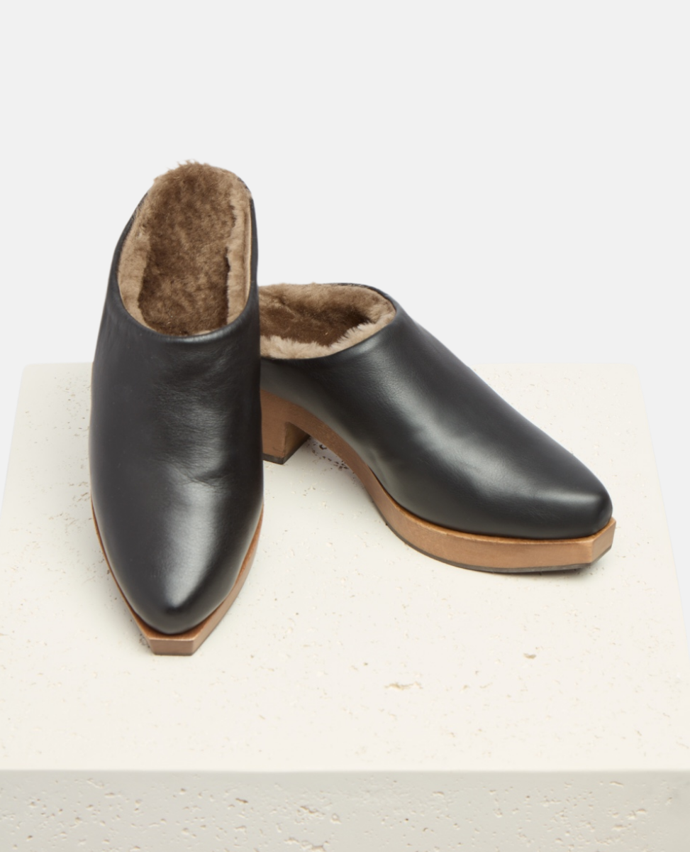 Pair of black leather clogs with brown soles on a light gray background