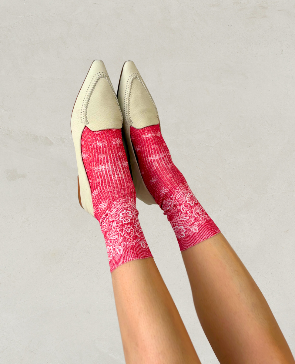 Pair of red socks with white paisley bandana pattern shown on the foot woth a pair of Coclico milk white pointed loafers