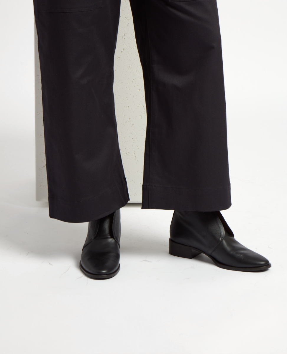 Black leather ankle boots with a sleek, smooth texture, featuring a low heel and rounded toe, paired with wide-leg black pants.