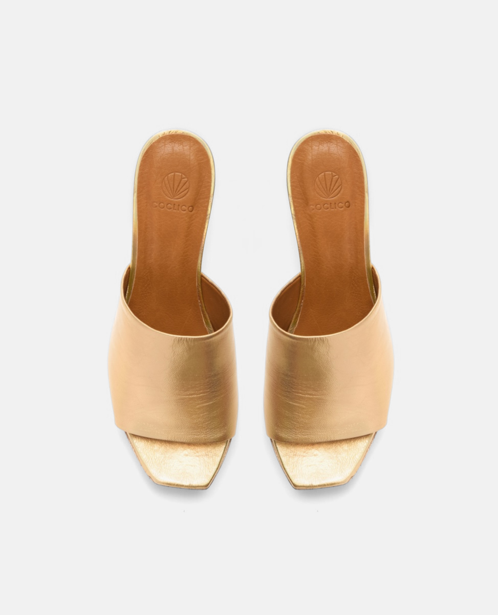 A pair of elegant, open-toed, gold metallic high-heeled mules with a square toe design and a smooth, shiny texture.