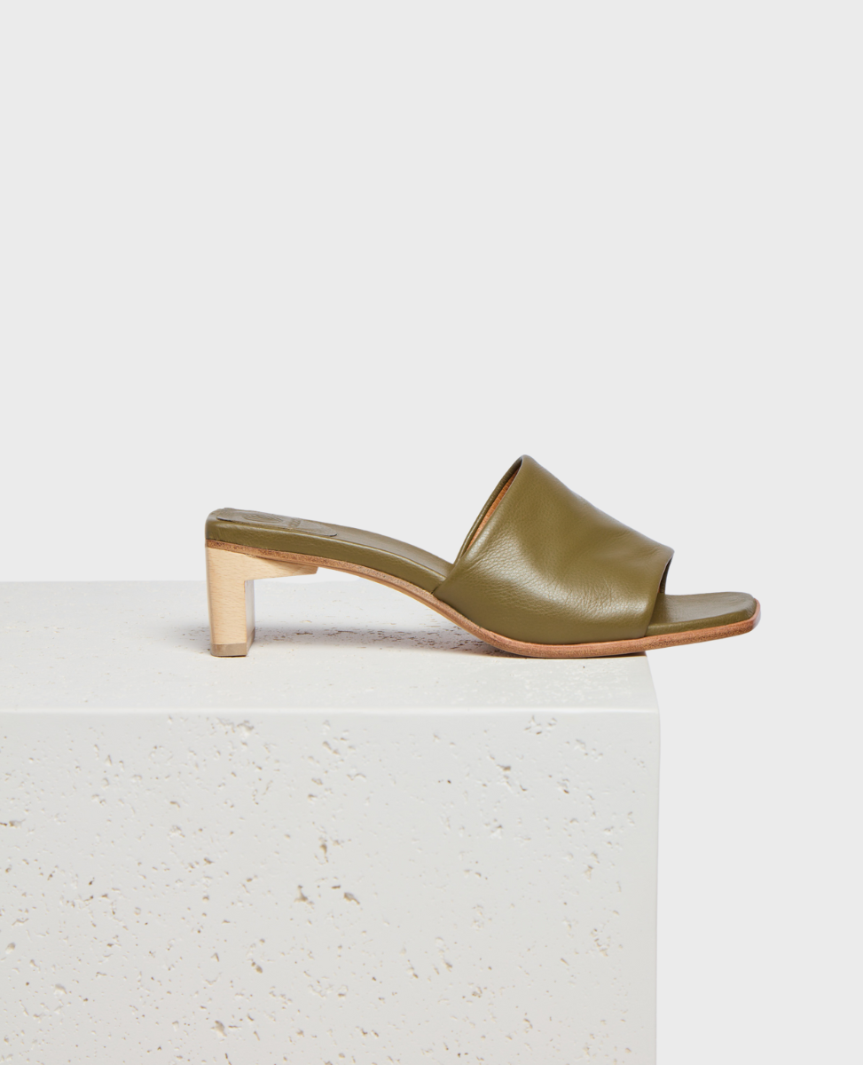 A sleek olive green leather mule with an open toe design, featuring a low wooden block heel and a smooth, minimalist finish.