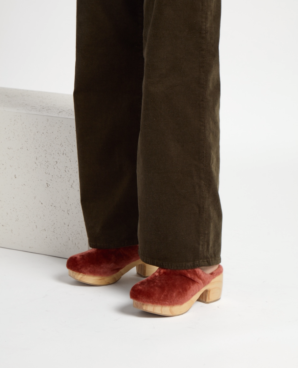 Pink red shearling clogs with a wooden sole and chunky heel, featuring a soft, textured upper and a classic slip-on design.