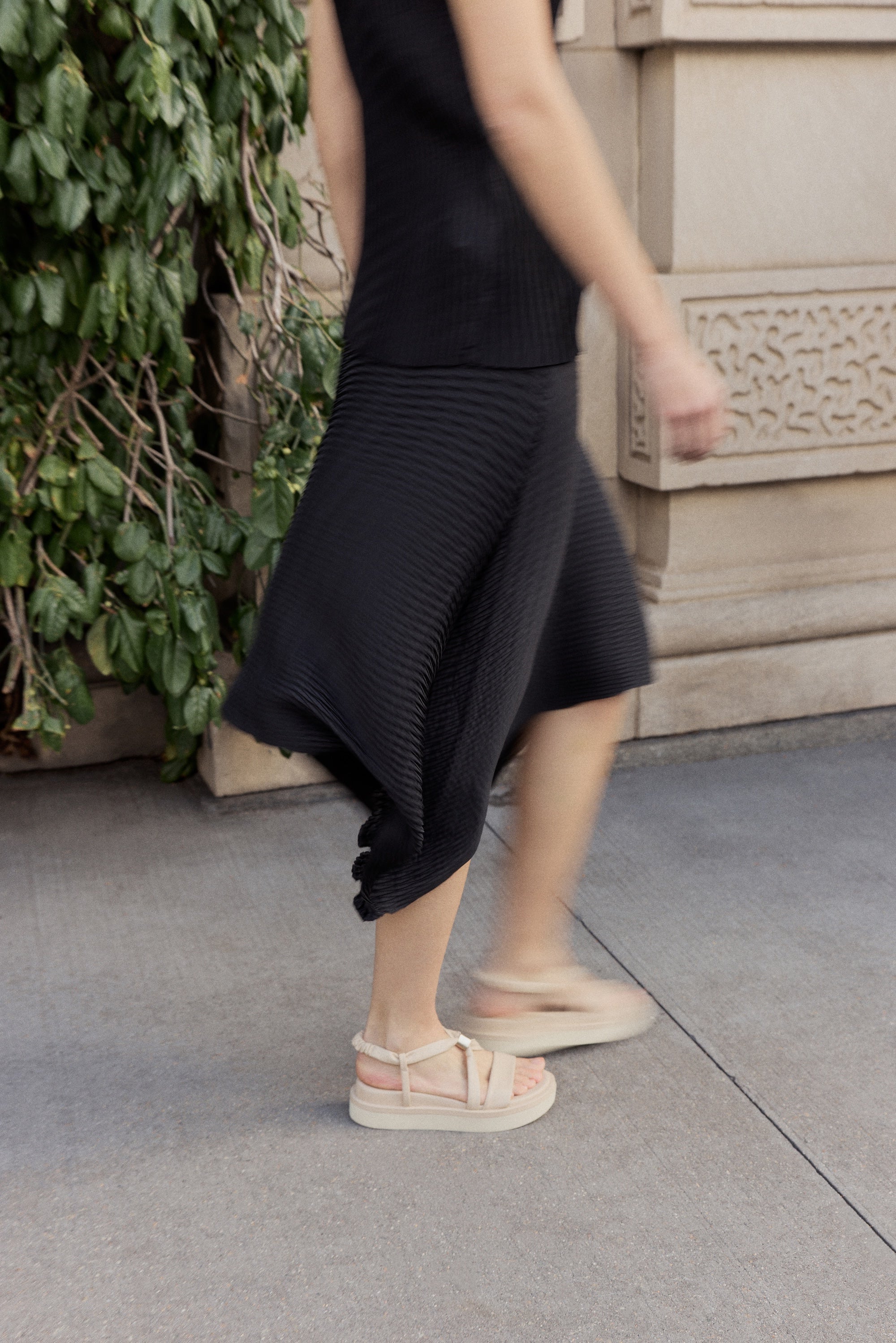 Woman walking in a black skirt and off white footbed wedge sandals