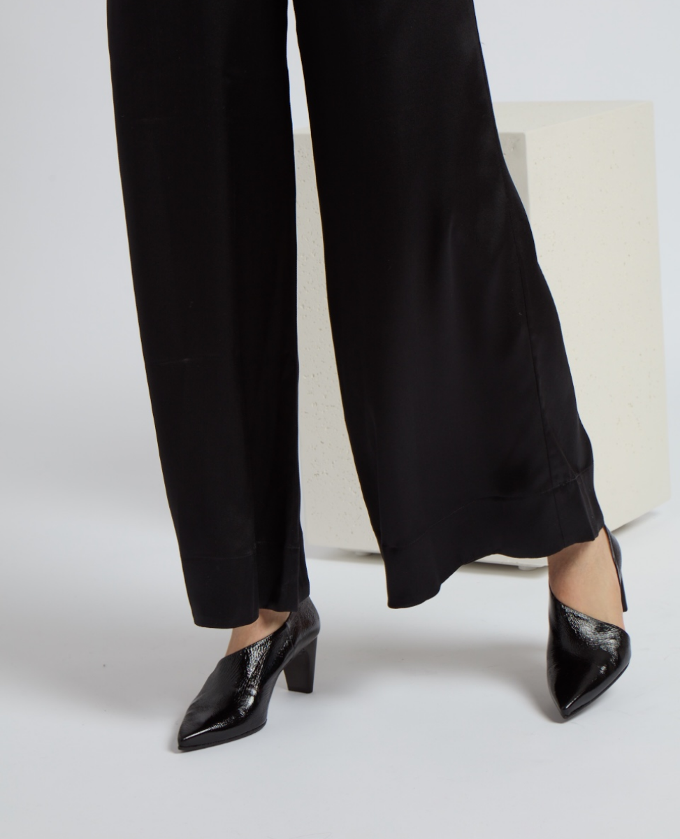 Black, pointed-toe shoes with a textured, glossy finish and a medium block heel, paired with loose-fitting black pants.