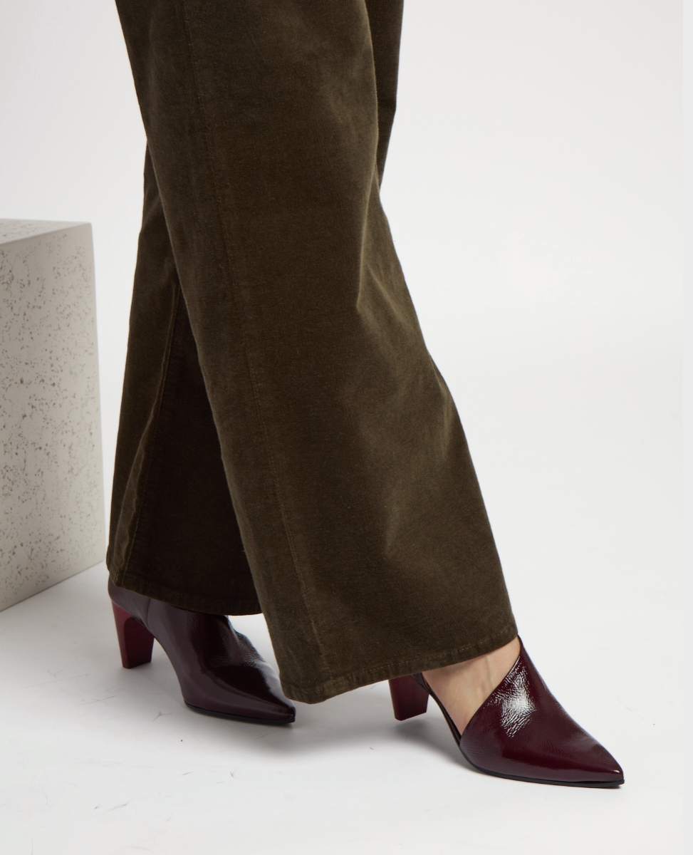 A pair of dark brown, wide-legged corduroy pants paired with glossy, burgundy pointed-toe wood-heeled shoes.