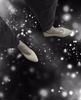 A pair of beige, pointed-toe flats with a glossy finish, featuring a mesh-like upper section and worn with black pants, set against a background of blurred, glowing white orbs on a dark surface. 13