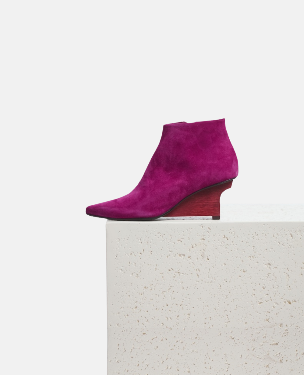 Purple suede ankle boot on a white pedestal with a white background
