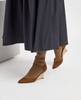 Person wearing brown wedge shoes and a long dark coat on a light background 5