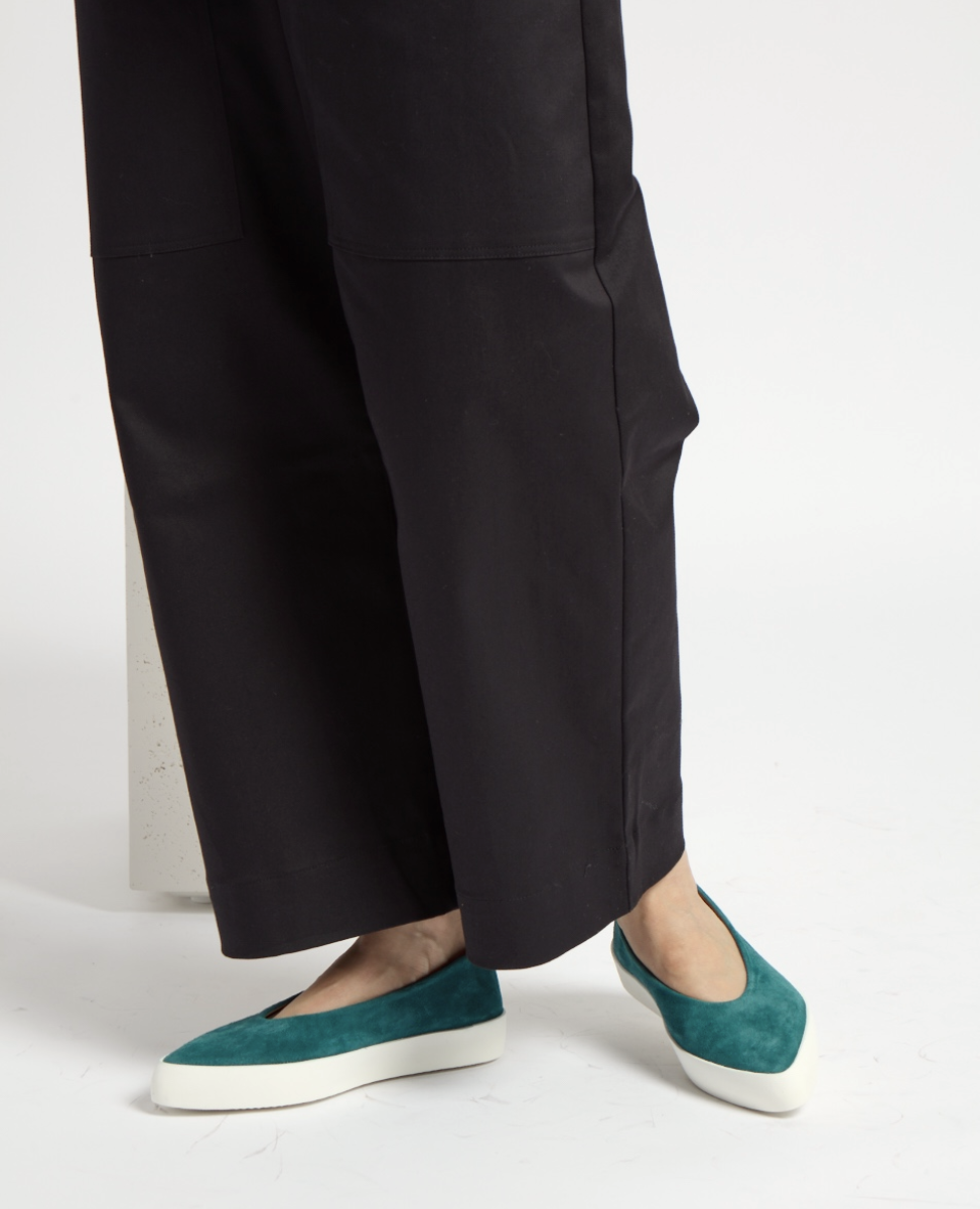 Teal suede slip-on shoes with a pointed toe and thick white rubber soles, worn with black wide-leg pants.