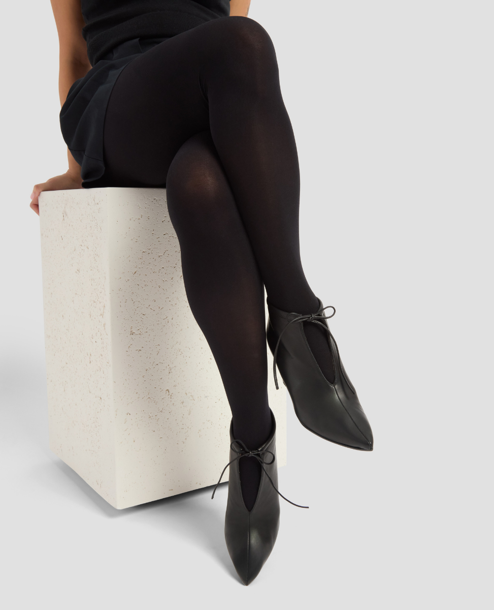 Person wearing black tights and shoes sitting on a white block against a light gray background