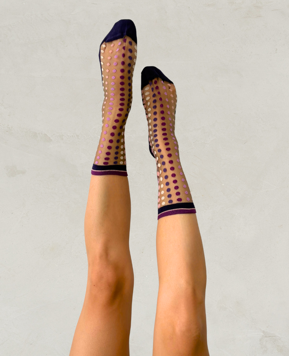 Sheer socks with polka dot pattern worn by a person on a plain background